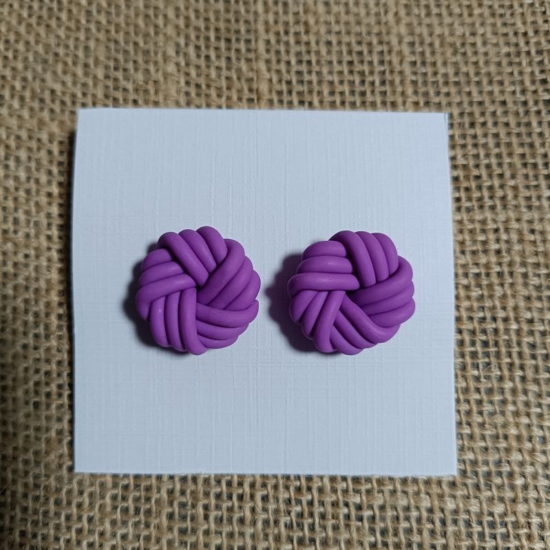 Purple polymer clay earrings in a knot design on a white card.