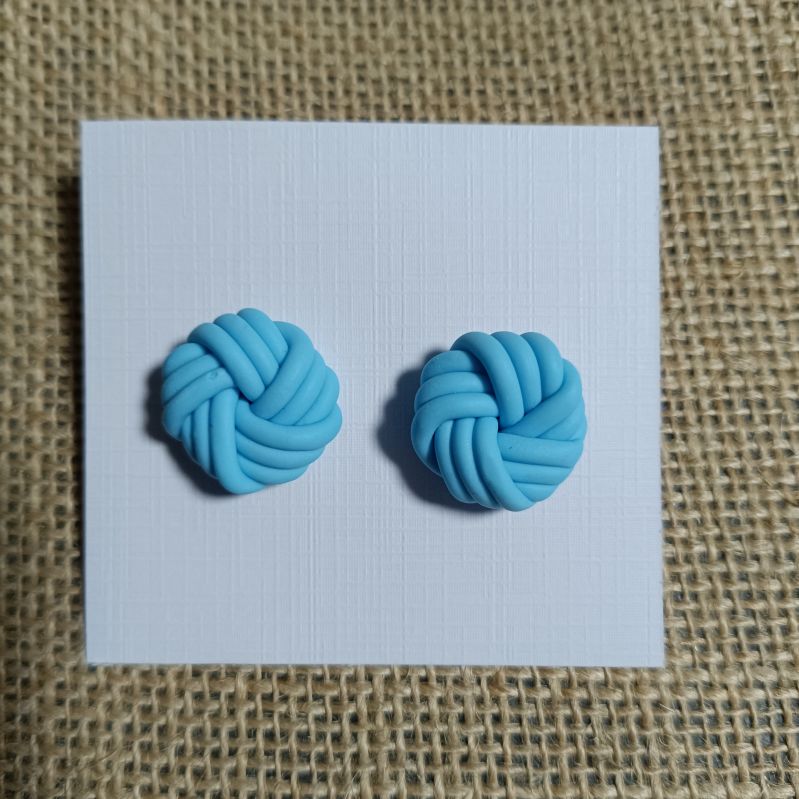 Handmade blue polymer clay knot earrings displayed on a white card.