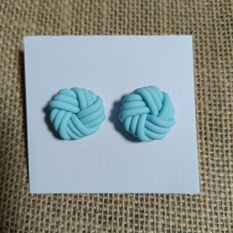 Light blue polymer clay earrings shaped like knots on a white card.
