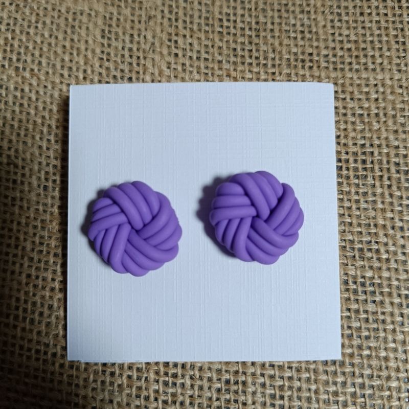 Purple polymer clay earrings shaped like knots on a white card.