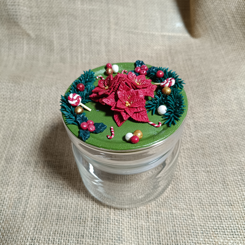Decorated glass jar with a green lid featuring red flowers and festive accents.