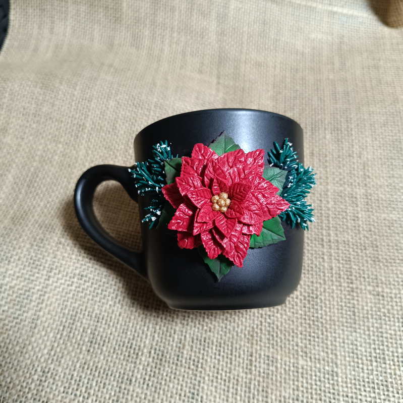 Black mug decorated with a red poinsettia and green leaves.