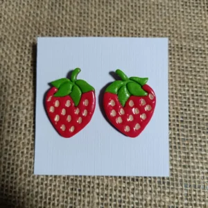 Red strawberry-shaped earrings with green leaves made from polymer clay.